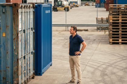 Homme comparant un container d'occasion rouillé et un container neuf dans un port industriel